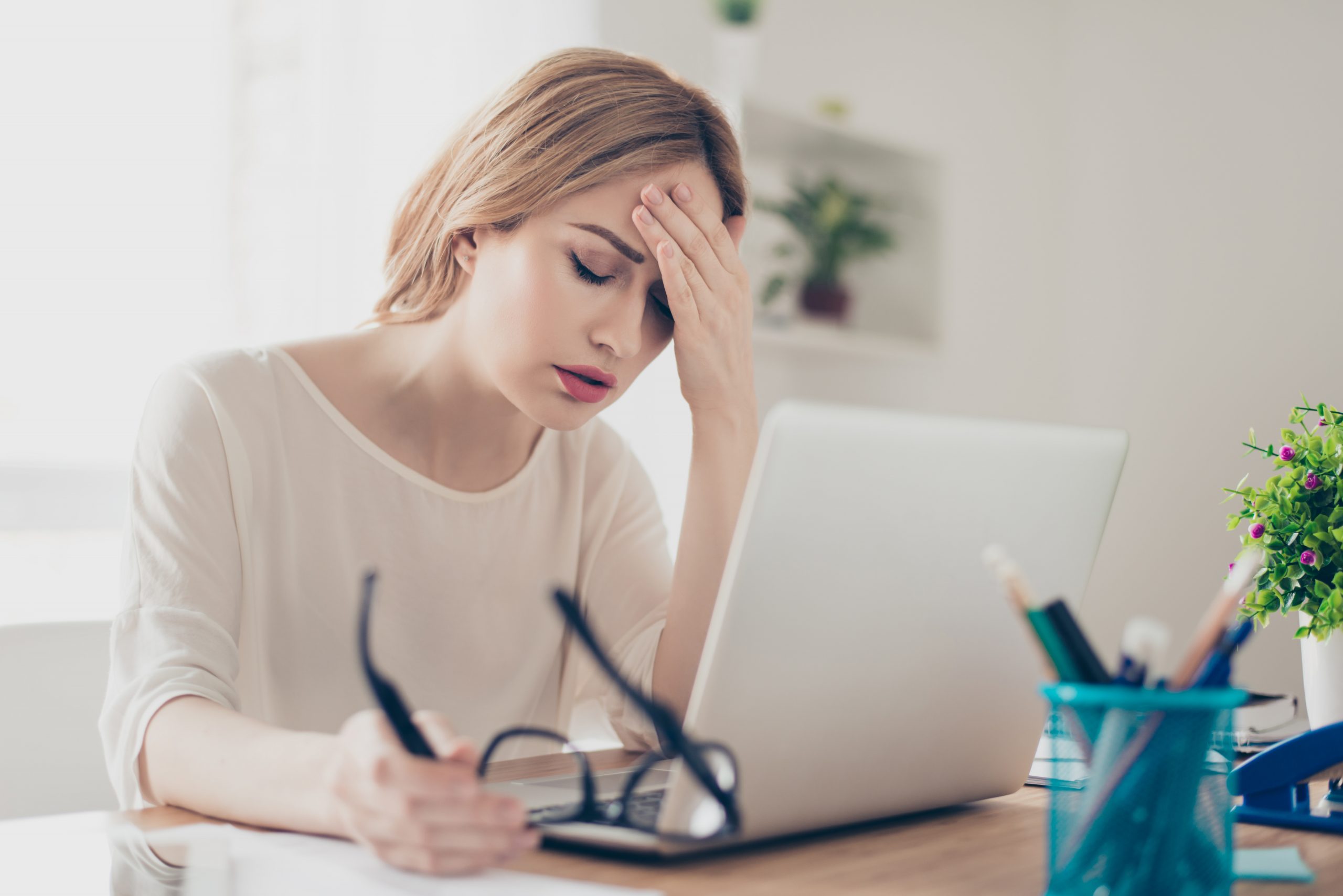 Stressed professional woman sitting at her desk, holding her head in frustration while working on a laptop, illustrating workplace stress and mental fatigue.